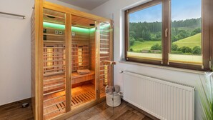 Eine Sauna mit Holzbänken und Blick auf eine grüne Landschaft durch ein Fenster.