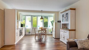 Eine moderne Küche mit Holzausstattung, einem Esstisch mit Stühlen und einem großen Fenster mit Blick auf Grünflächen.