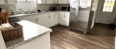 Una cocina moderna con armarios blancos, electrodomésticos de acero inoxidable y un suelo de madera en patrón de espiga.