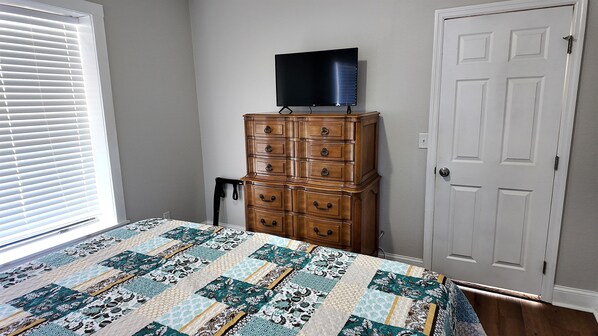 Un dormitorio con cama, cómoda, televisor y puerta.