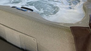 Un jacuzzi con cubierta de madera y una casa al fondo.