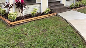 Una casa de un piso con un porche cubierto, una puerta principal y un pequeño jardín con diversas plantas.