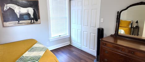 Une chambre à coucher avec un lit, une commode, un miroir, un tableau représentant un cheval et une porte fermée.