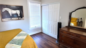 Un dormitorio con una cama, un aparador, un espejo, un cuadro de un caballo y una puerta cerrada.