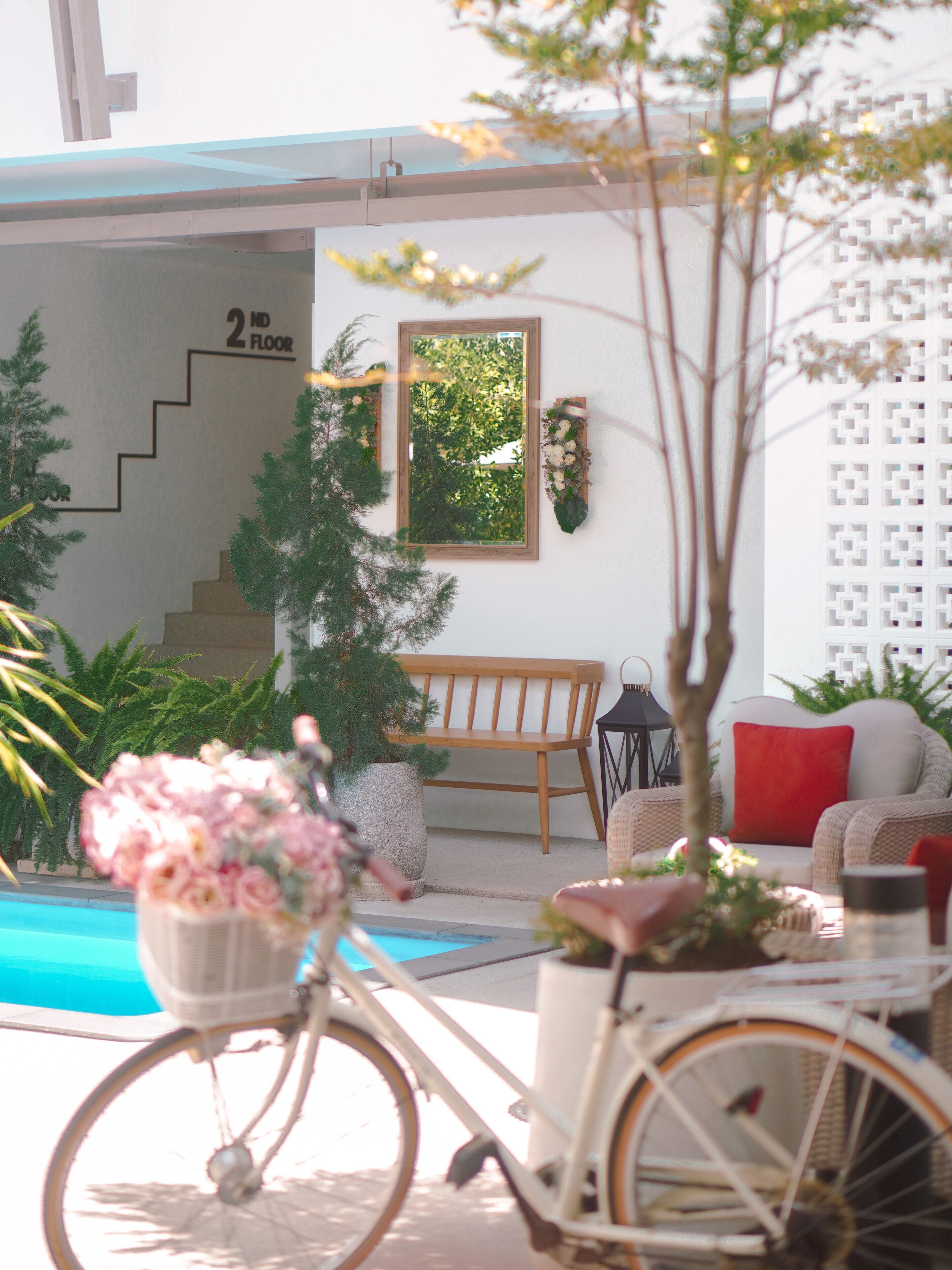 A bicycle with a basket, a bench, a chair, a small table, and a potted plant near a pool.