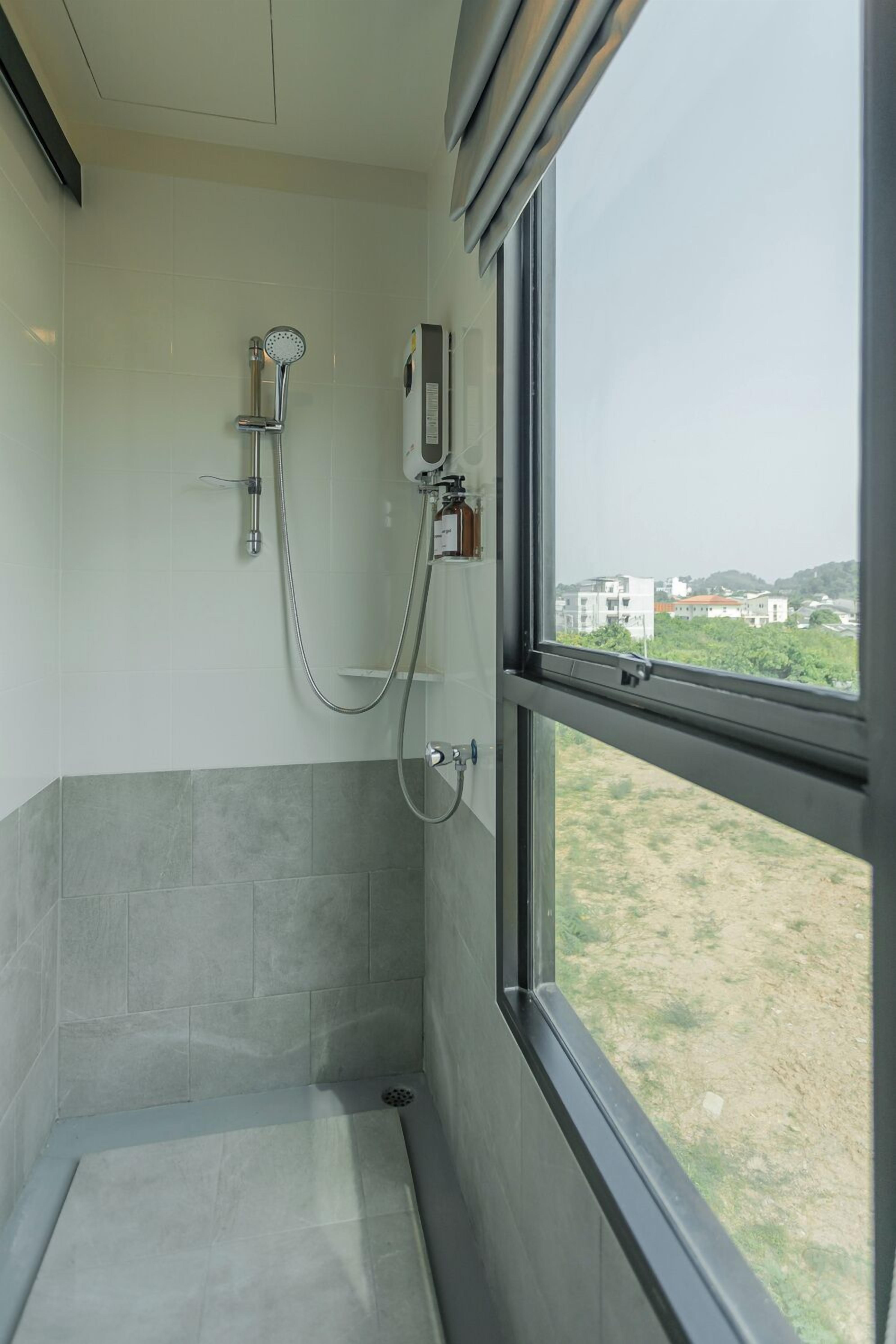 Une salle de bain avec une douche, une fenêtre et une vue sur les bâtiments et la verdure environnante.