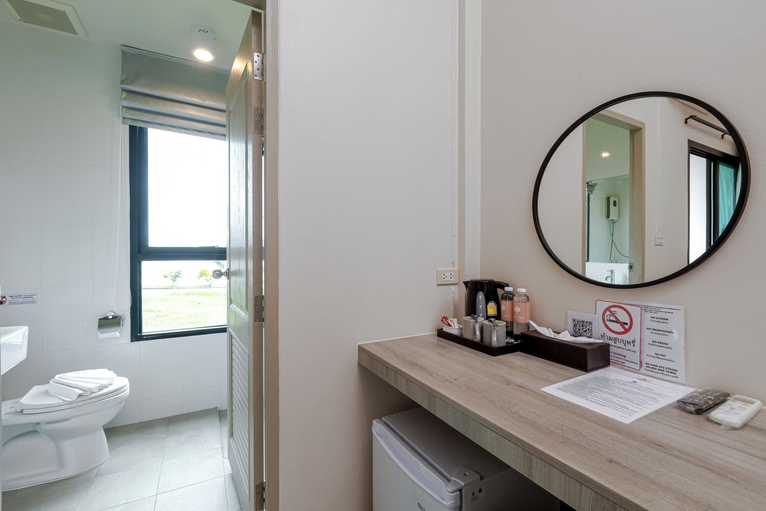 A bathroom with a toilet, sink, mirror, and a window.