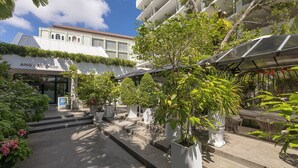 Un patio de hotel con plantas en macetas, asientos exteriores y un edificio con un letrero que dice