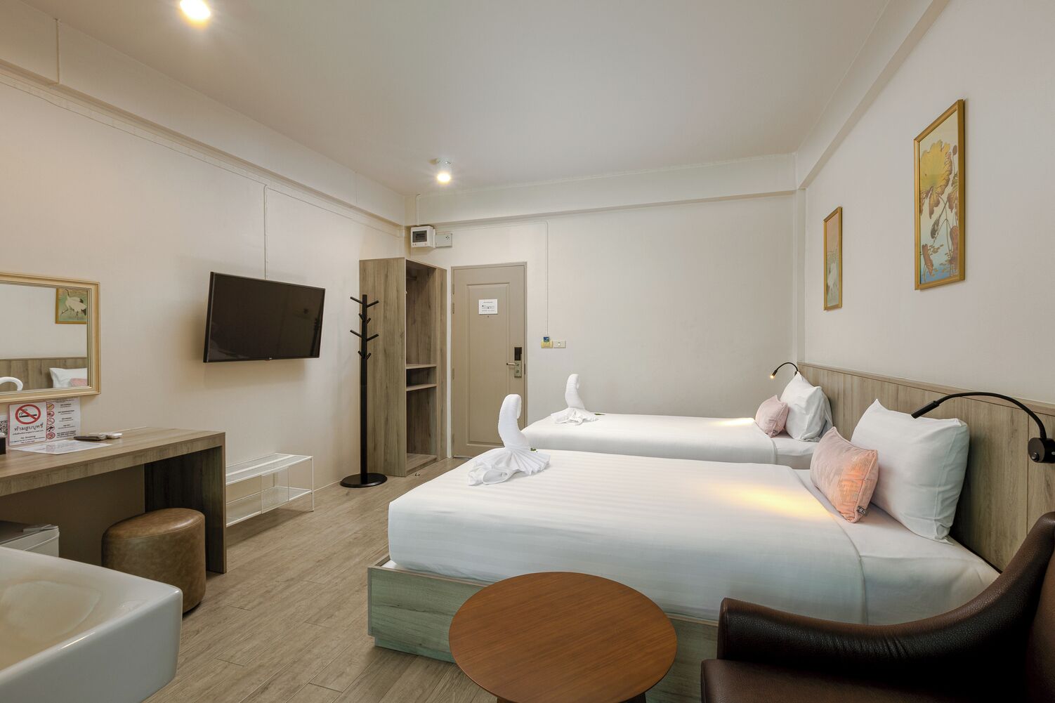 Habitación de hotel con dos camas, un escritorio, una silla, una mesa redonda, un televisor y un perchero.
