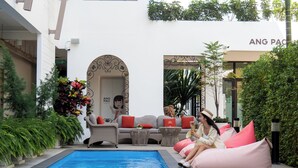 Zona junto a la piscina con mobiliario de mimbre y pufs, un letrero que dice 'ANG PAO HOTEL', y una escalera que lleva a un nivel superior.
