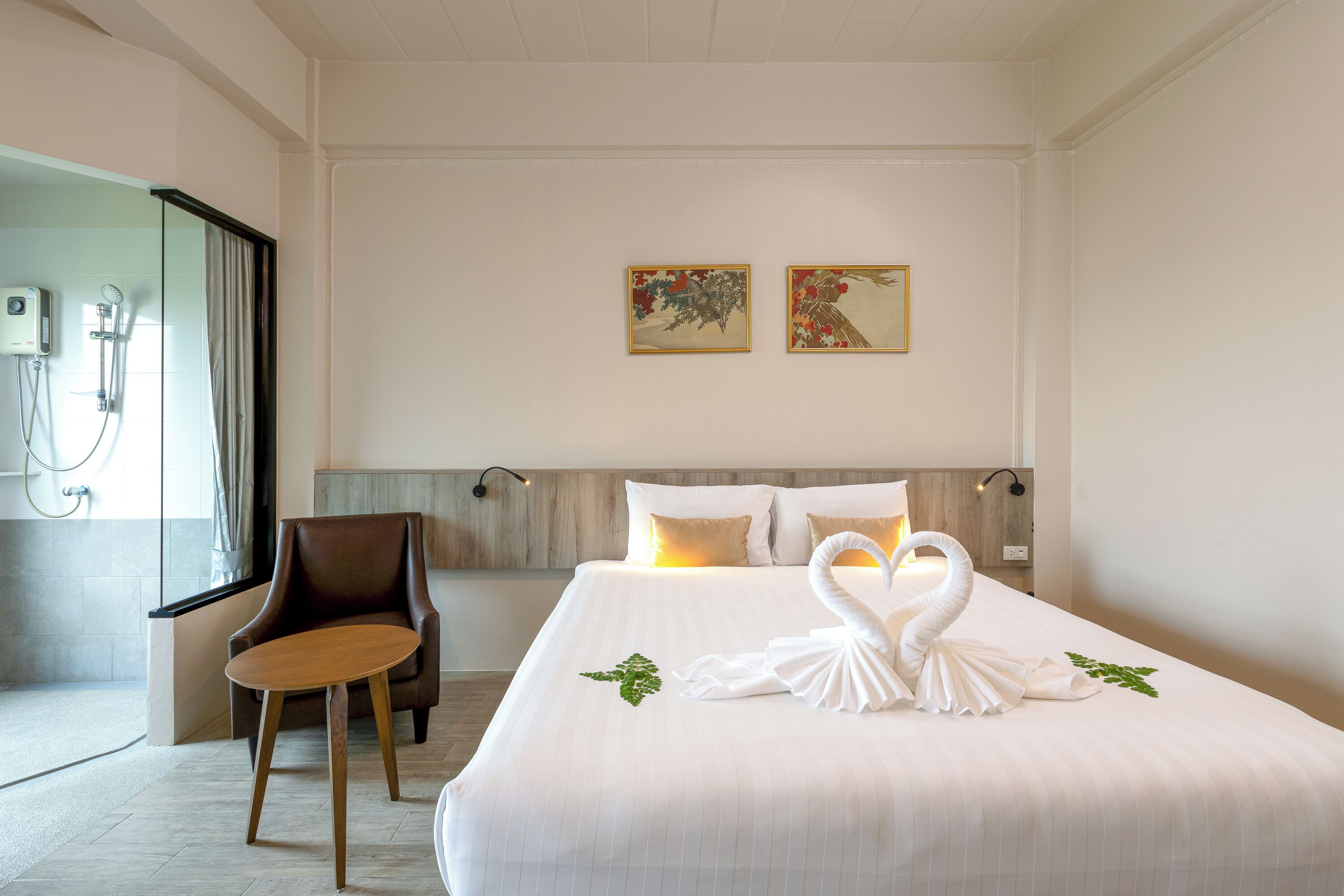 A hotel room with a large bed, a chair, a shower area, and two framed artworks on the wall.