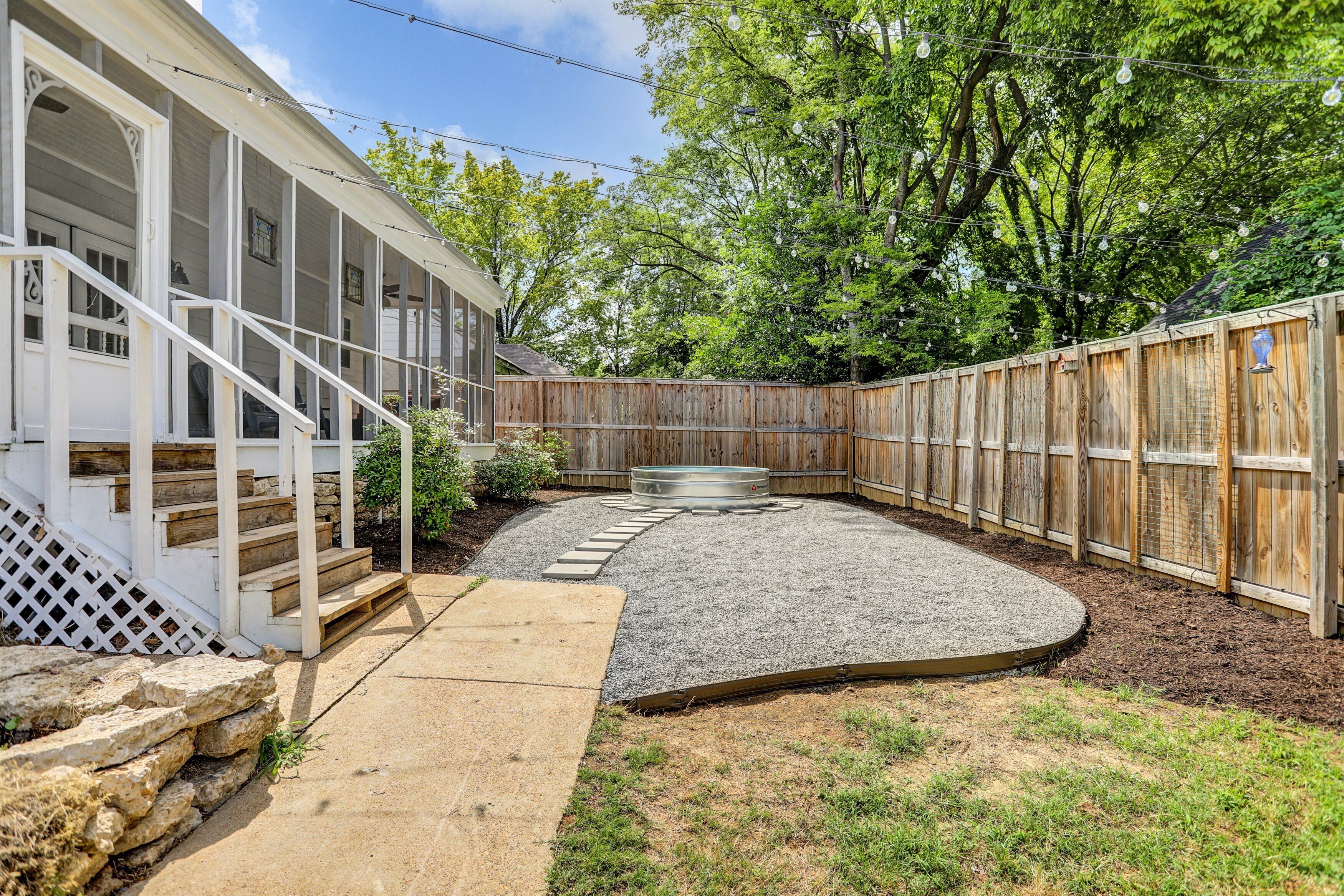 A backyard with a wooden deck, a stone wall, and a fenced area.