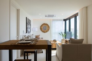 A modern living room with a dining area, a round mirror, and large windows.