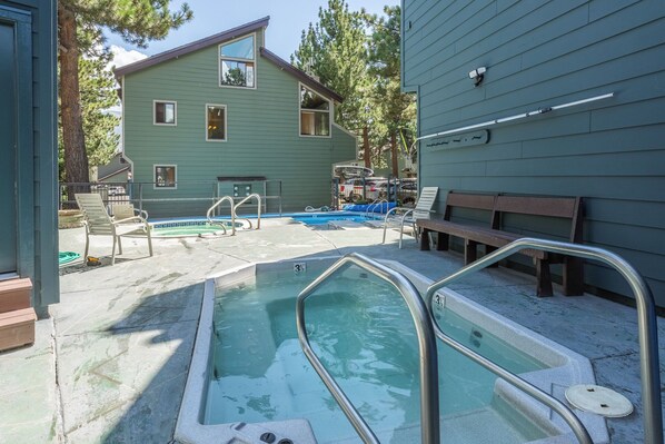 A pool area with a hot tub, lounge chairs, and a building in the background.