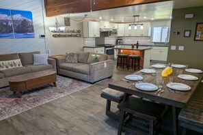 A modern living room with a sofa set, a coffee table, and a dining area with a wooden table set for a meal. - Newly Updated 2BR w/loft 3BA Family Ski Basecamp 568 (Mammoth Lakes)