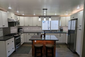 A modern kitchen with white cabinets, a central island with stools, a stainless steel refrigerator, and a microwave. - Newly Updated 2BR w/loft 3BA Family Ski Basecamp 568 (Mammoth Lakes)
