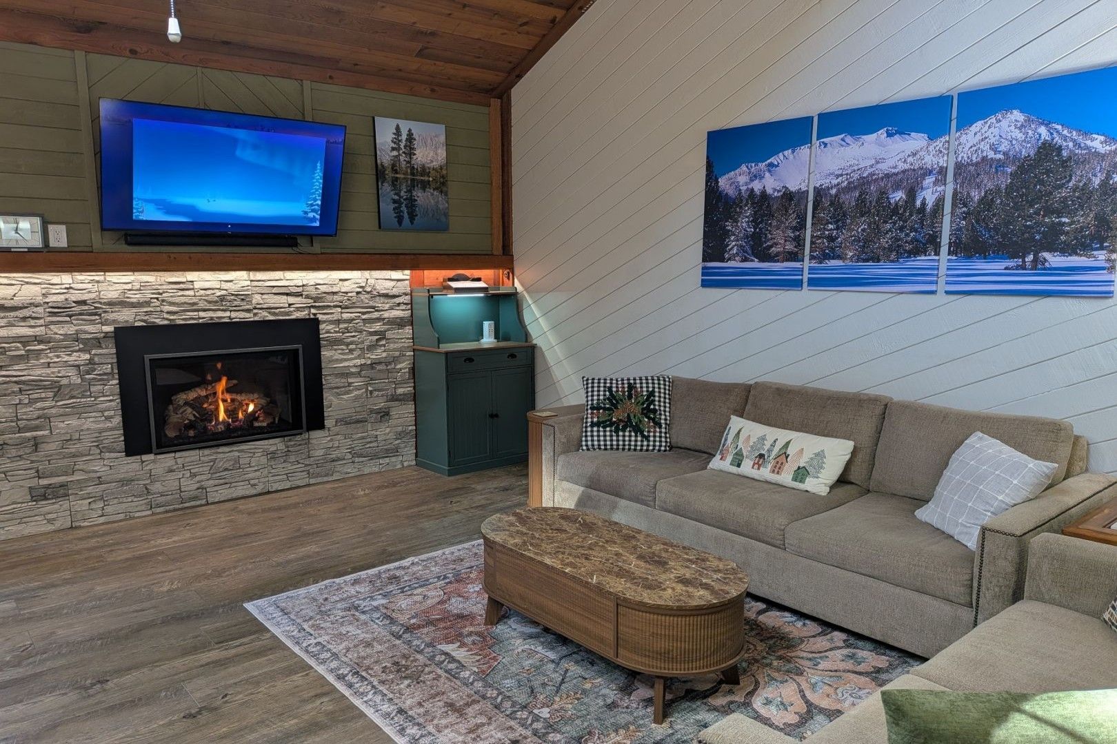A cozy living room with a stone fireplace, a flat-screen TV, and a large window with a mountain view.