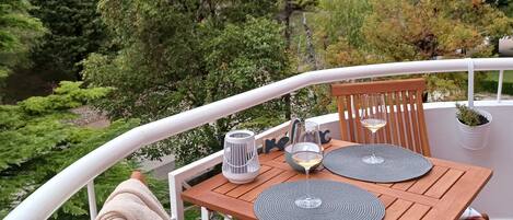 A wooden table set with two glasses and a candle on a balcony with a white railing.