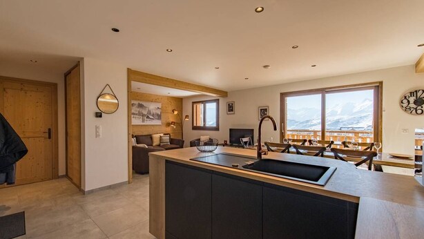 Una cocina moderna con una isla central, armarios de madera y grandes ventanales con vistas a la montaña.