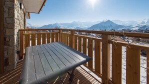 Terraza de madera con una mesa, con vistas a un paisaje montañoso nevado.