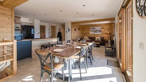 Un comedor amplio con una larga mesa de madera y sillas, una cocina al fondo y un ventanal grande a la derecha.