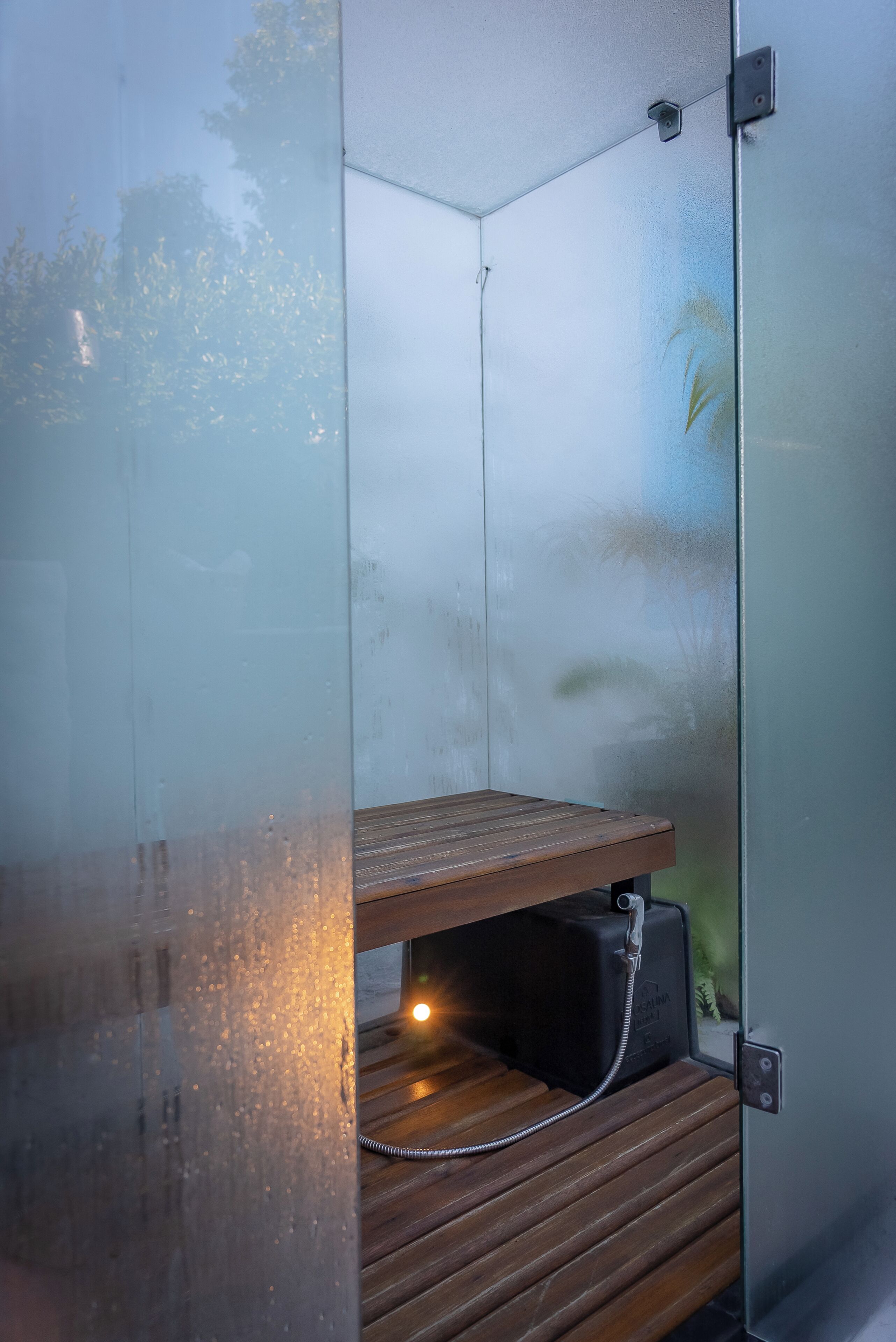 A glass-enclosed shower with a wooden bench, a visible water pipe, and a wall-mounted light fixture.