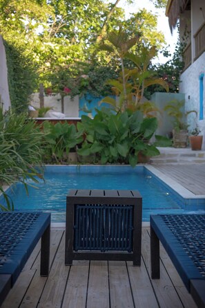 A wooden deck with a pool, surrounded by lush greenery and a building with blue accents. - Pousada Bem te vi trancoso (Porto Seguro)