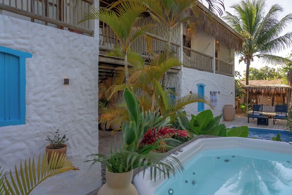 A pool area with a hot tub, potted plants, and a building with a balcony. - Pousada Bem te vi trancoso (Porto Seguro)