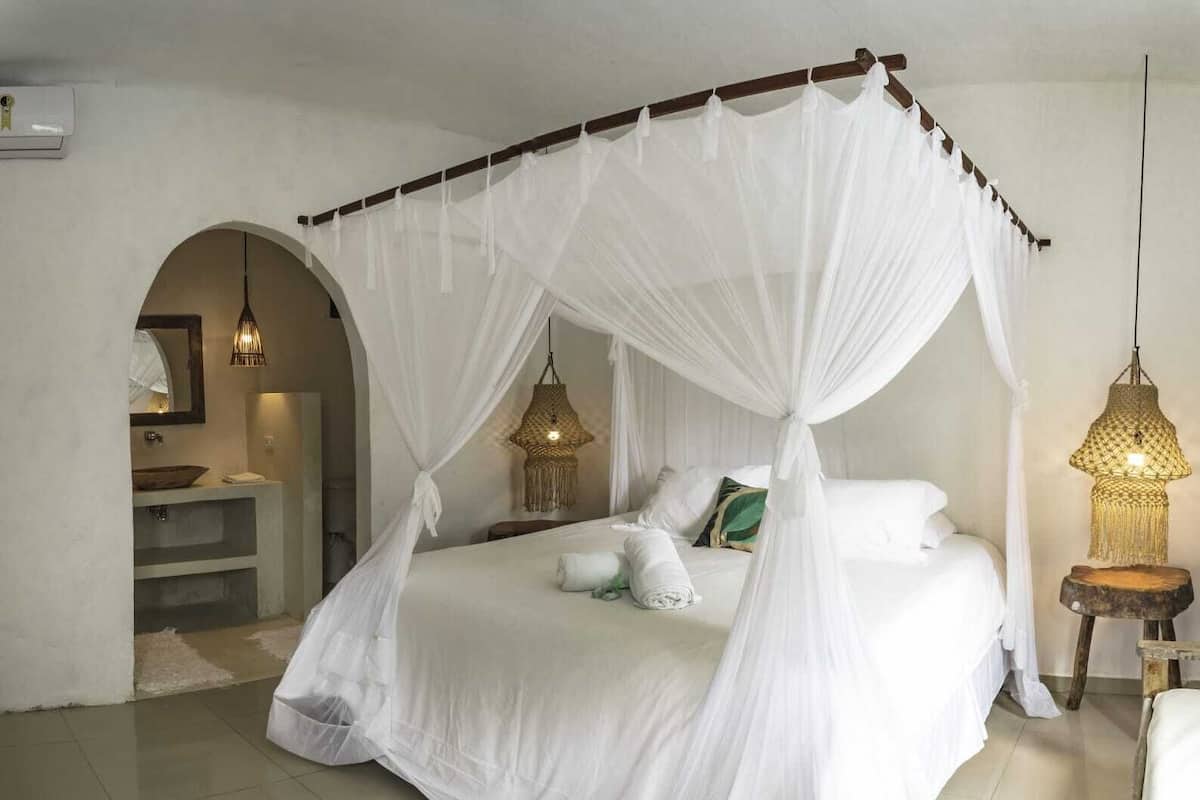 Quarto com cama de dossel, mesa de cabeceira pequena, luminária pendente e espelho.