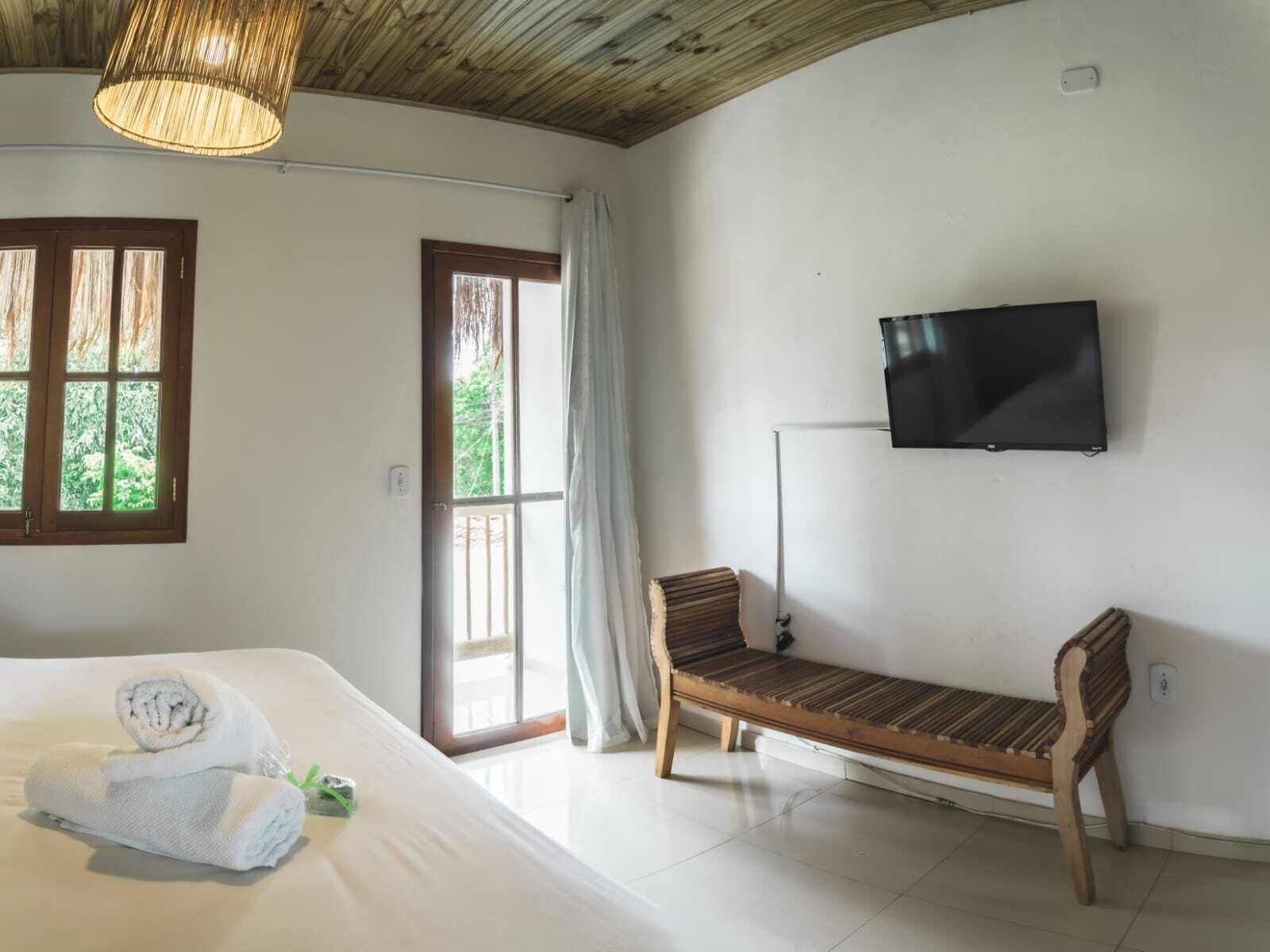 A bedroom with a bed, a bench, a TV, and a window with curtains.