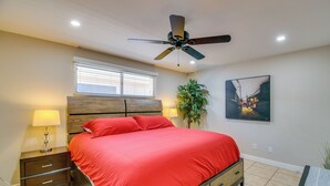 Una camera da letto con un letto, un comodino, una lampada, una ventola a soffitto, una finestra e un quadro appeso al muro.