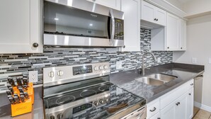 Una cucina moderna con elettrodomestici in acciaio inossidabile, una parete di fondo rivestita di piastrelle e mobili in legno bianco.