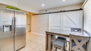 Una cucina con un frigorifero in acciaio inox, un dispenser per l'acqua, un tavolo da pranzo con piano in vetro e due sedie, e una porta scorrevole in stile rustico.