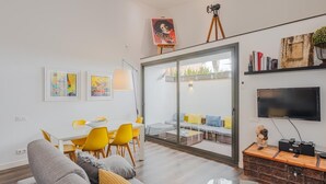 A modern living room with a sofa, dining table, chairs, a glass coffee table, a TV, and a bookshelf. - Loft Miro Apart Barcelona (Barcelona)