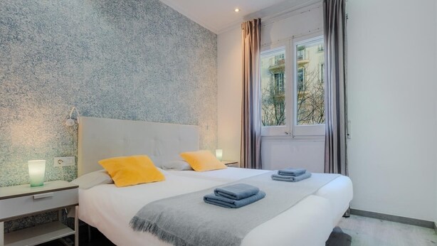 A modern bedroom with a large bed, a nightstand, a bedside table, and a window with curtains.