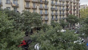 A multi-story residential building with balconies, parked cars, and trees in the foreground.