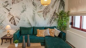 A living room with a green sectional sofa, a wooden coffee table, a lamp, and a wall mural. - Sound Of The Mountain Chania (Chania)