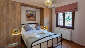 A bedroom with a bed, bedside tables, a window with a view, and a painting on the wall. - Sound Of The Mountain Chania (Chania)
