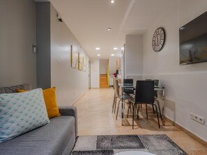 Uma sala de estar moderna com um sofá, uma área de jantar com cadeiras, um relógio na parede e uma escada ao fundo.