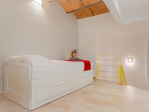 Quarto com cama, extintor de incêndio, escada amarela e uma pequena janela.