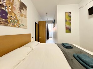 A hotel room with a large bed, a wooden headboard, a painting on the wall, and a view into the hallway.