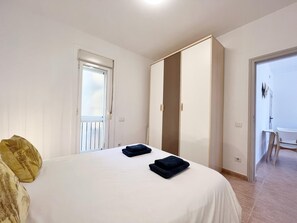 Une chambre à coucher comprenant un lit, deux oreillers, une armoire et une porte donnant sur une autre pièce.