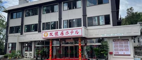 Un hotel con alfombra roja en la entrada, ventanas amplias y un letrero en idioma extranjero.