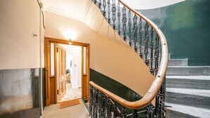 Een brede, statige trap met versierde metalen leuningen en een houten handrail, die uitkomt in een goed verlichte gang.