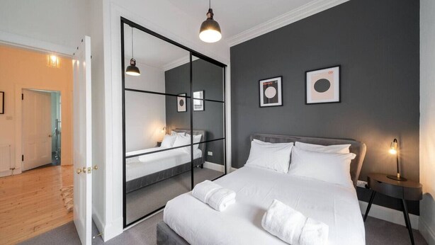 Een moderne slaapkamer met een groot bed, een nachtkastje, een spiegel en een wandlamp.
