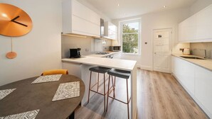 Een moderne keuken met witte kasten, een centraal eiland en een zithoek met twee barkrukken.