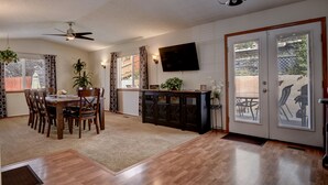 A dining area with a wooden table and chairs, a ceiling fan, and a TV mounted on the wall. - Spacious 5 BDR 3 BA House with Hot Tub, BBQ, Fire Pit, Home Gym, Mountain View (Colorado Springs)