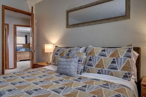 A bedroom with a patterned bedspread, a bedside lamp, and a mirror on the wall. - Spacious 5 BDR 3 BA House with Hot Tub, BBQ, Fire Pit, Home Gym, Mountain View (Colorado Springs)