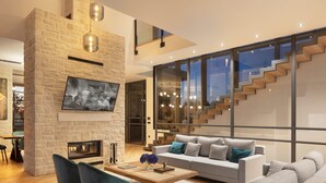 Una sala de estar moderna con una chimenea de piedra, un televisor de pantalla plana grande y una escalera que lleva a un nivel superior.