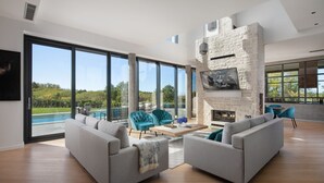 Amplia sala de estar con chimenea de piedra, ventanas grandes y vista a la piscina.